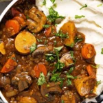 A bowl of vegan lentil and mushroom stew garnished with fresh herbs.